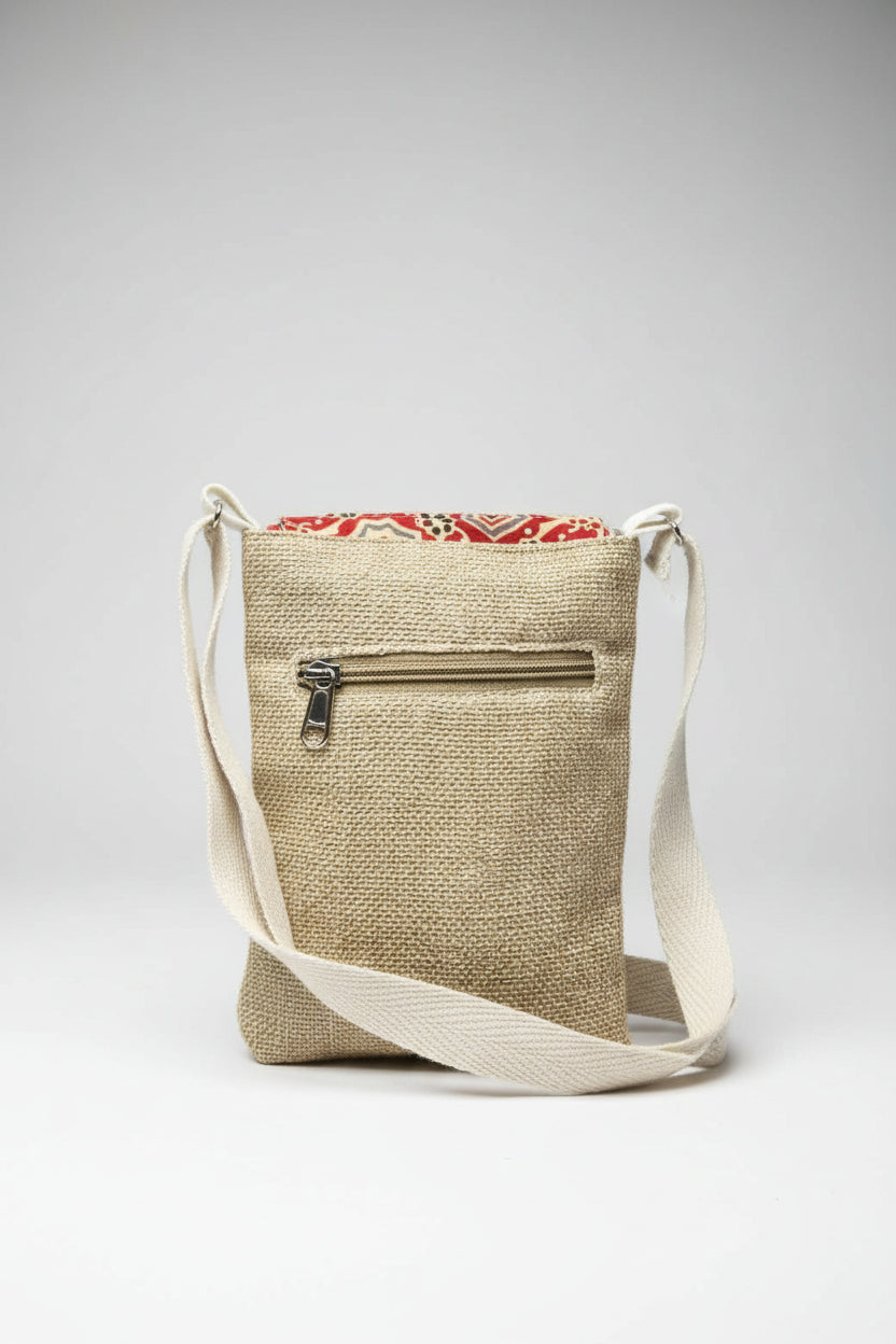  woven natural fiber crossbody bag with a beige body, cream strap, and a red patterned flap peeking out at the top, shown on a white background.
