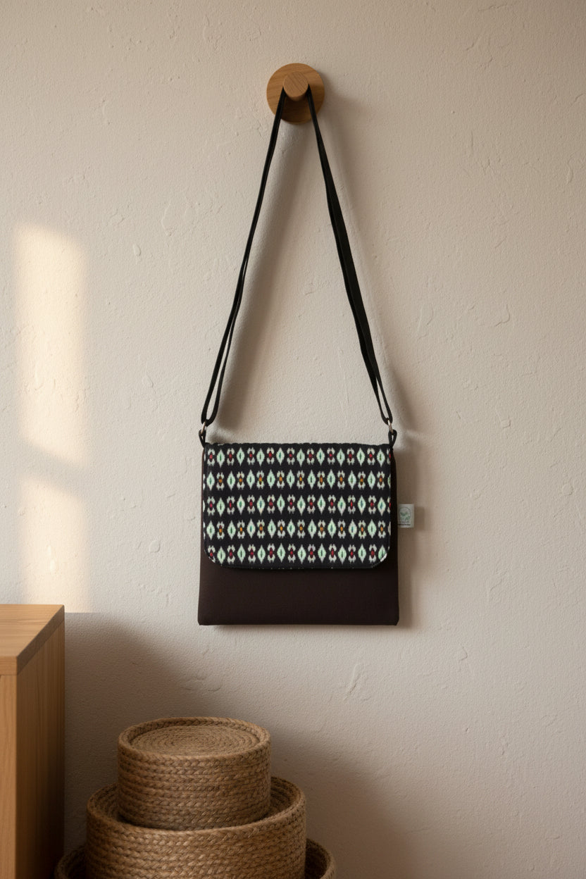 Black crossbody bag with  ikkath patterned flap on a white background